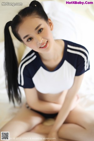 A woman in a blue and white shirt is sitting on a bed.