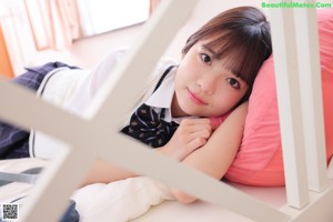 A young woman sitting on a bed holding a pink pillow.