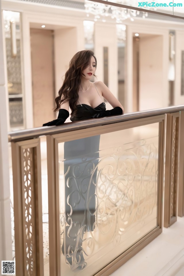 A woman in a black dress standing on a balcony.