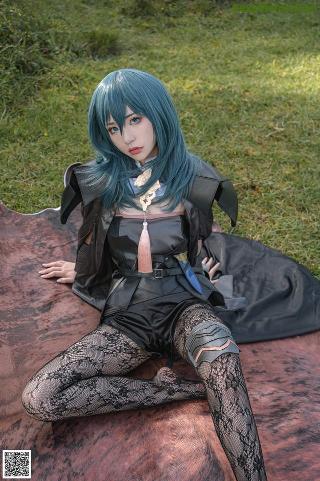 A woman with blue hair sitting on a blanket in the grass.