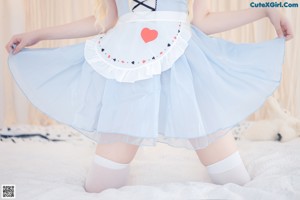 A woman in a blue dress and white stockings is standing by a window.