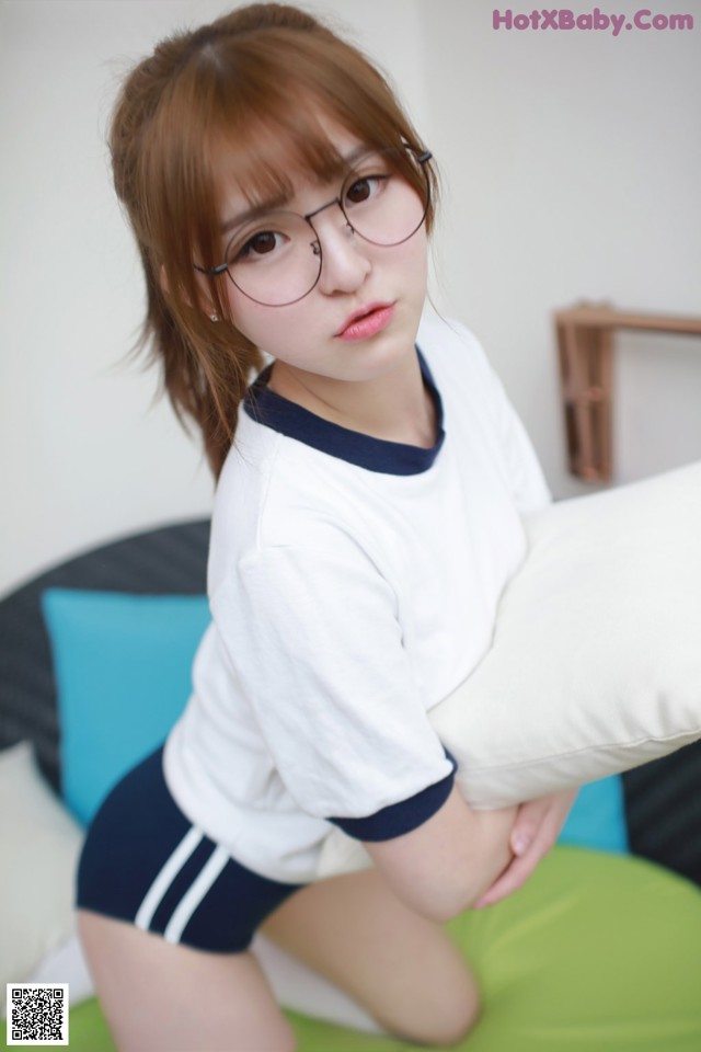 A young woman wearing glasses sitting on a bed.