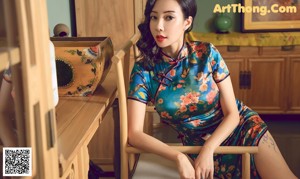 A woman in a blue dress sitting on a wooden chair.