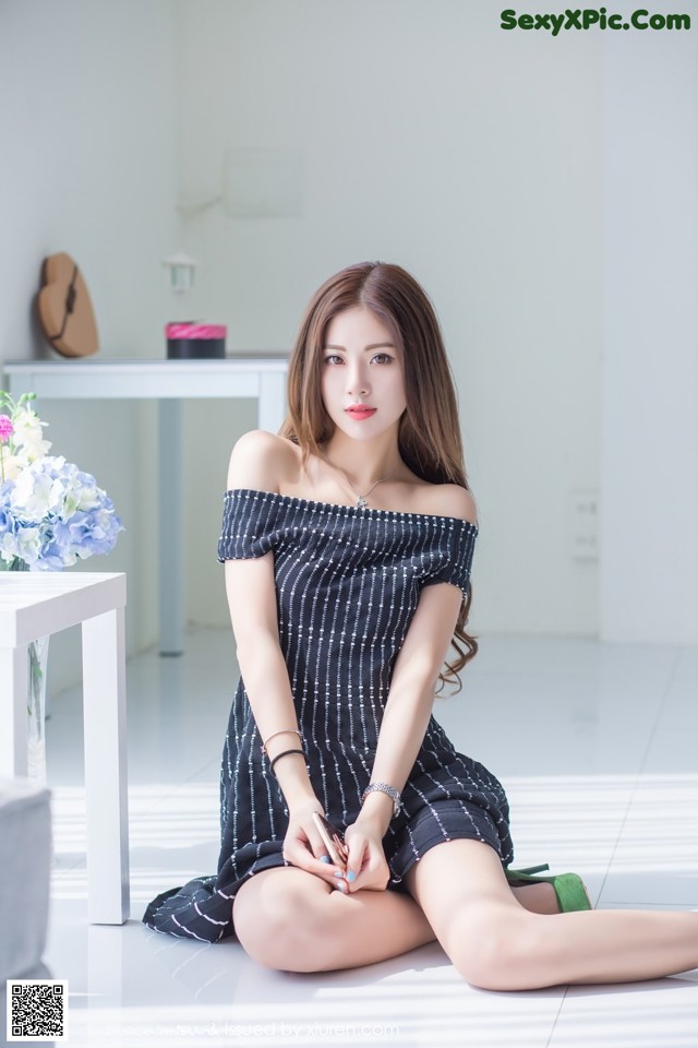 A woman sitting on the floor in a black and white dress.