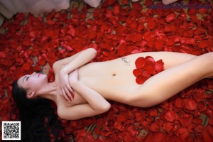 A woman in a black bikini laying on a bed of rose petals.