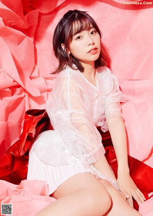 A woman sitting on a bed in a pink sweater.