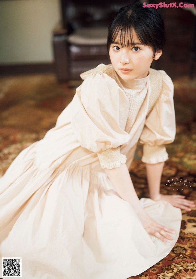 A woman in a white dress sitting on a rug.