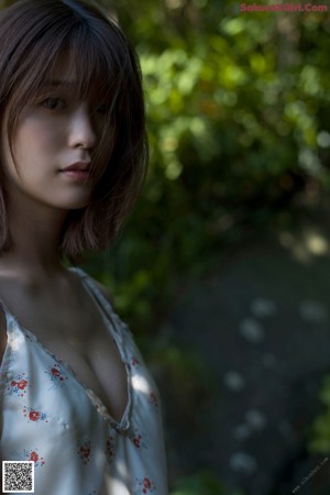 A woman standing in front of a lush green forest.