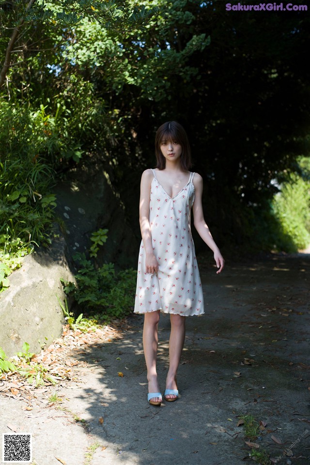 A woman in a white dress standing on a dirt road.