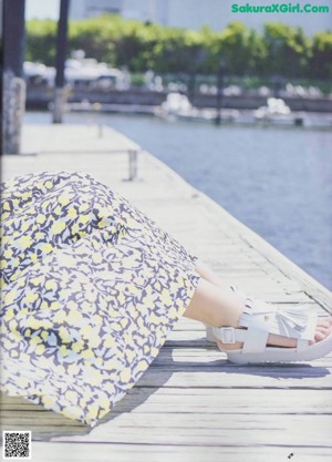 A woman in a floral dress sitting on a dock.