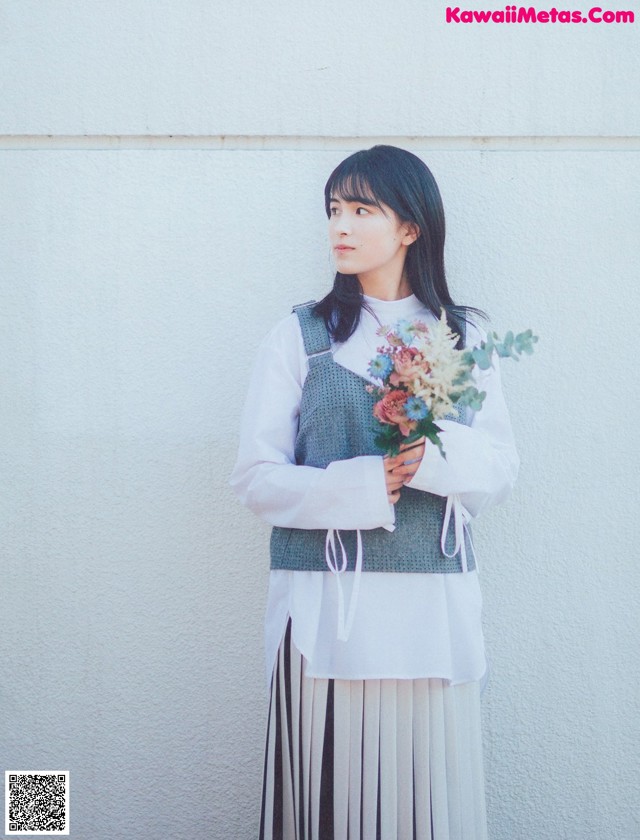 A woman standing in front of a white wall holding a bouquet of flowers.