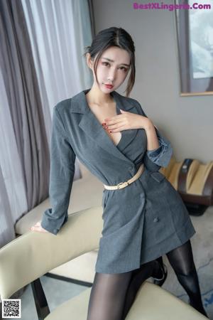 A woman in a gray suit and black tights posing for the camera.