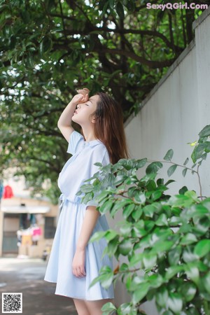 A woman sitting on the ground in front of a bush.