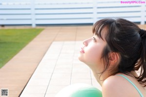 A woman in a green swimsuit sitting on a pink ball.