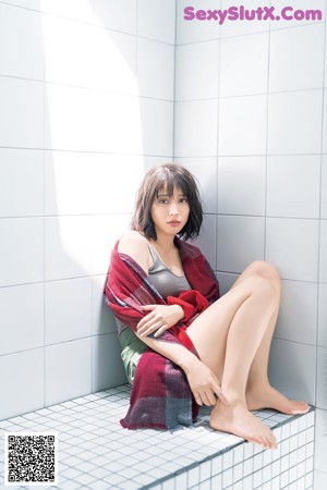 A woman sitting on a tiled floor with her legs crossed.