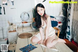 A woman in a pink and white striped bodysuit sitting on a stool.